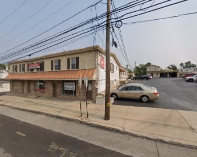 Two-story beige building with orange awning on a street with parked cars.