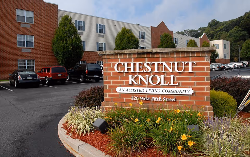 Brick sign reads Chestnut Knoll in front of a multi-story assisted living building.