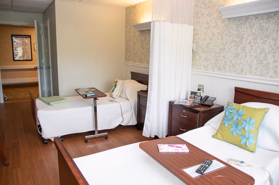 Two hospital-style beds separated by a privacy curtain in a warmly lit patient room.