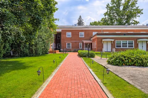 Brick walkway leads to the entrance of a red brick senior living facility.