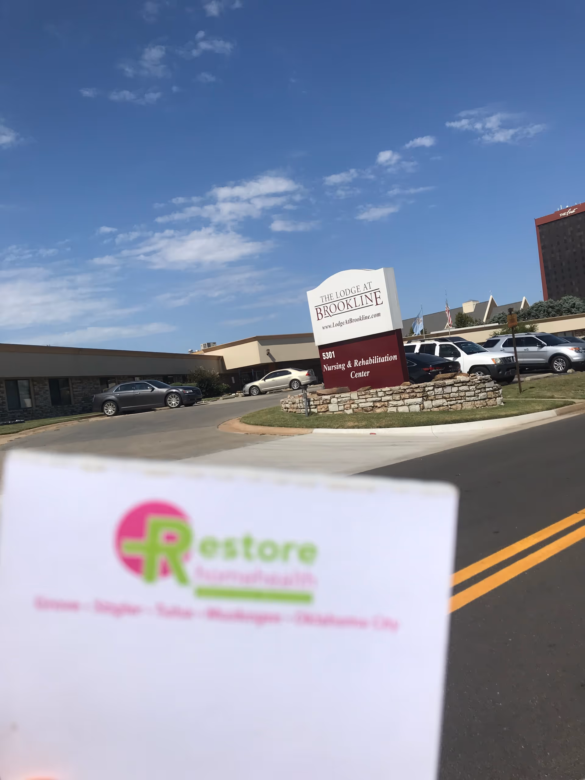 Exterior view of a nursing and rehabilitation center with a front sign, cars, and blue sky.