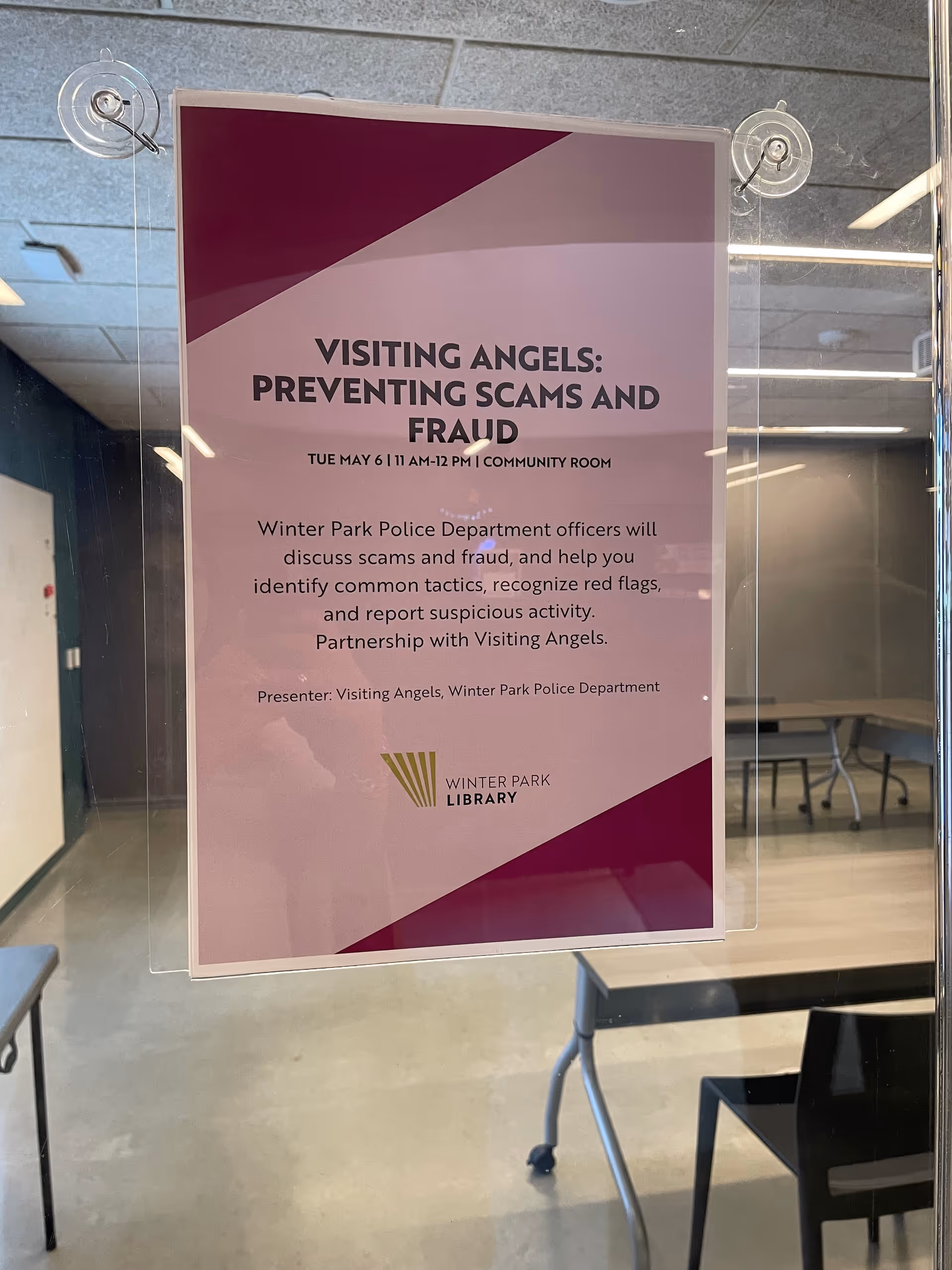 Poster reading Visiting Angels: Preventing Scams and Fraud hangs on a glass door in a hall.
