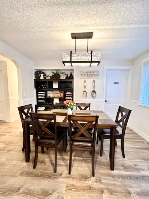 A dining room with a dark wooden table, chairs, decorative shelf, and sign.