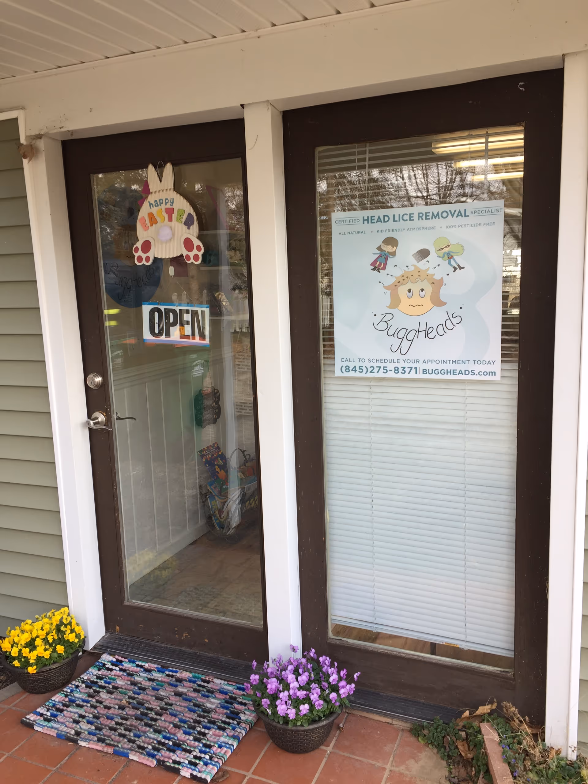 Front entrance with glass doors, a welcome mat, potted flowers, and a BuggHeads sign.