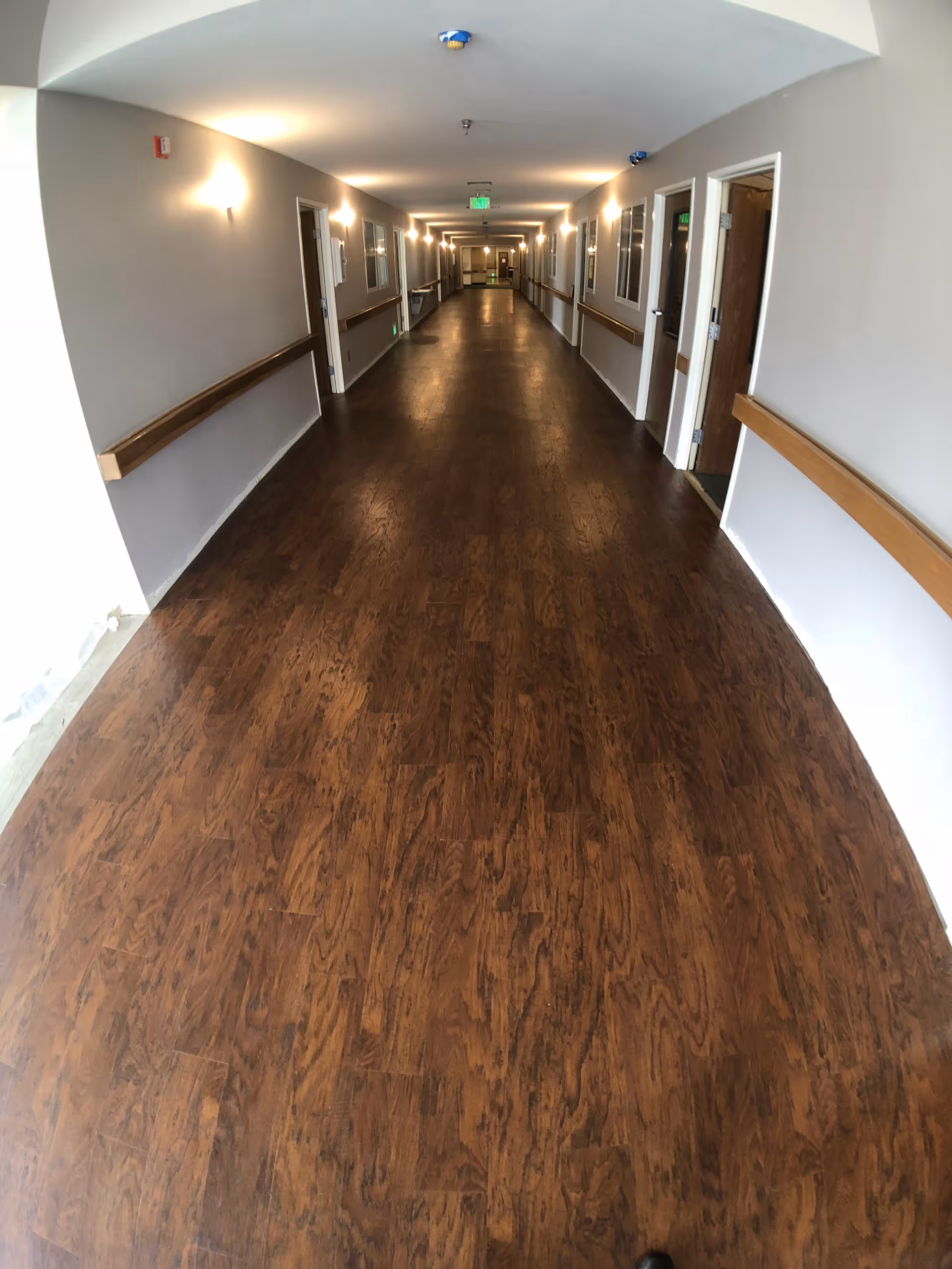 Long indoor corridor with wood floors, wall handrails, and closed doors along both sides.