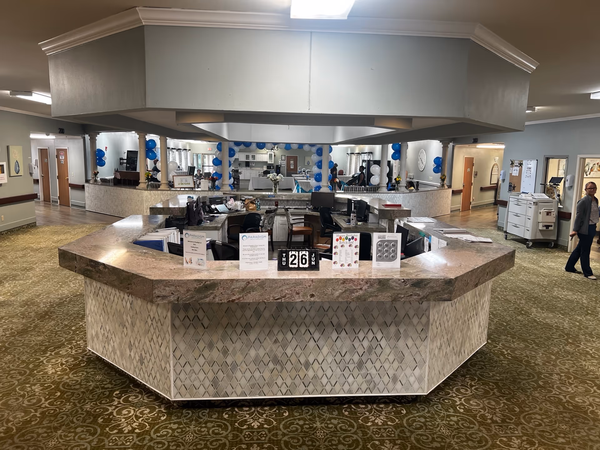 Wide view of a curved reception desk in a spacious nursing home lobby with blue balloons.