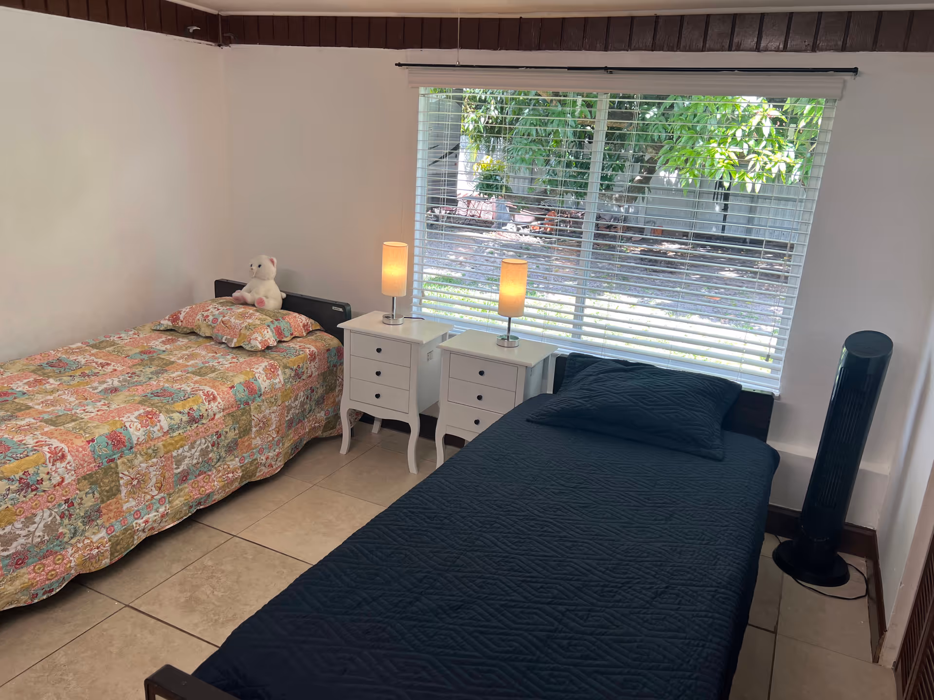 Two single beds with nightstands and a window in a bright, tidy bedroom.
