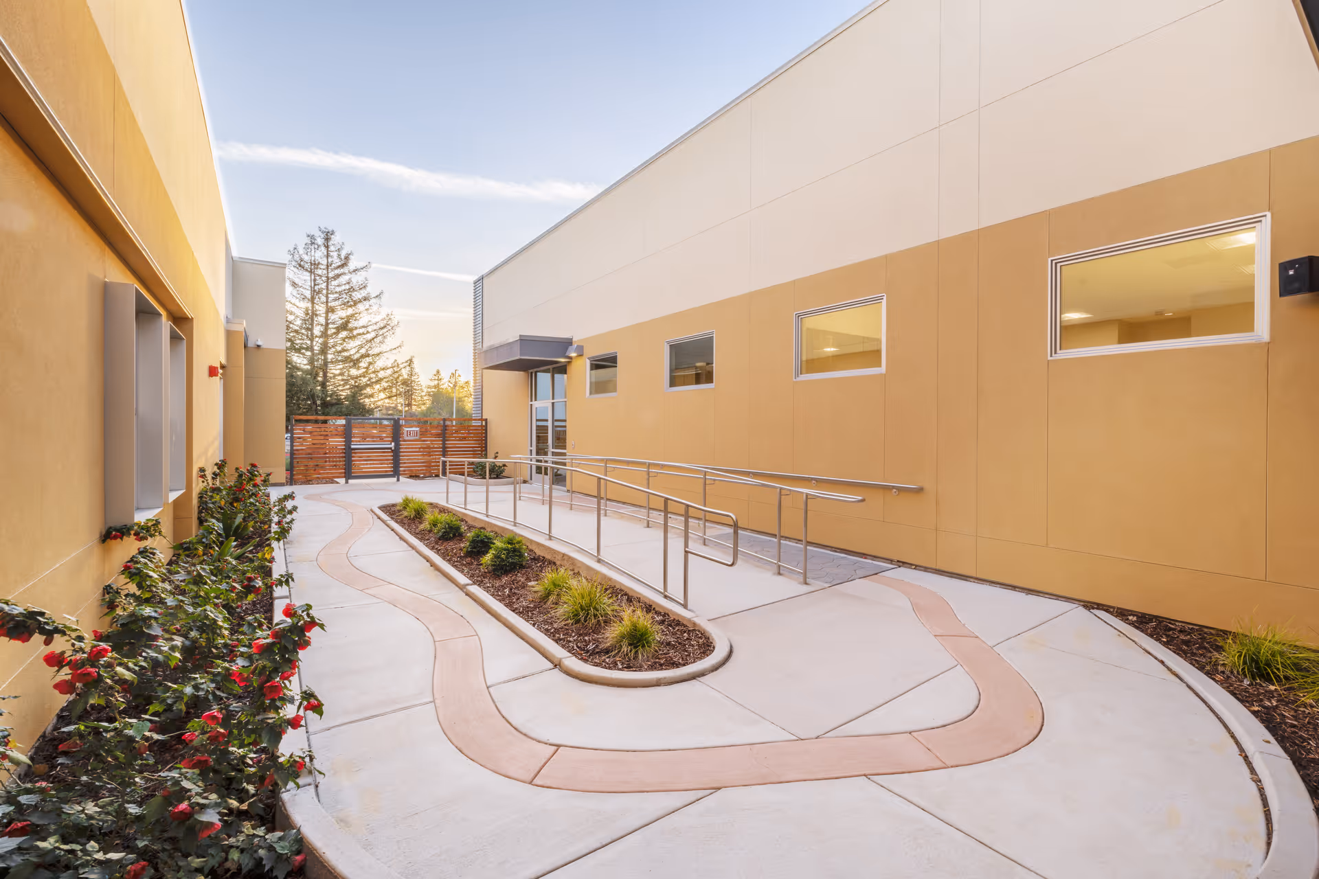Sunny exterior courtyard at Shadelands Post Acute with curved path, rails, and garden beds.