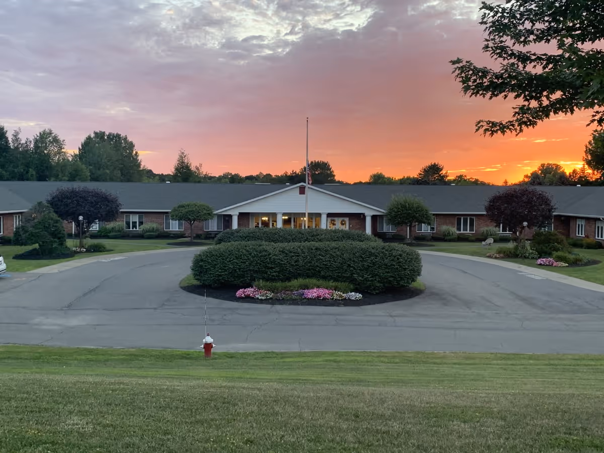 Wide view of Elderwood Village at Colonie front entrance with circular drive and landscaping.
