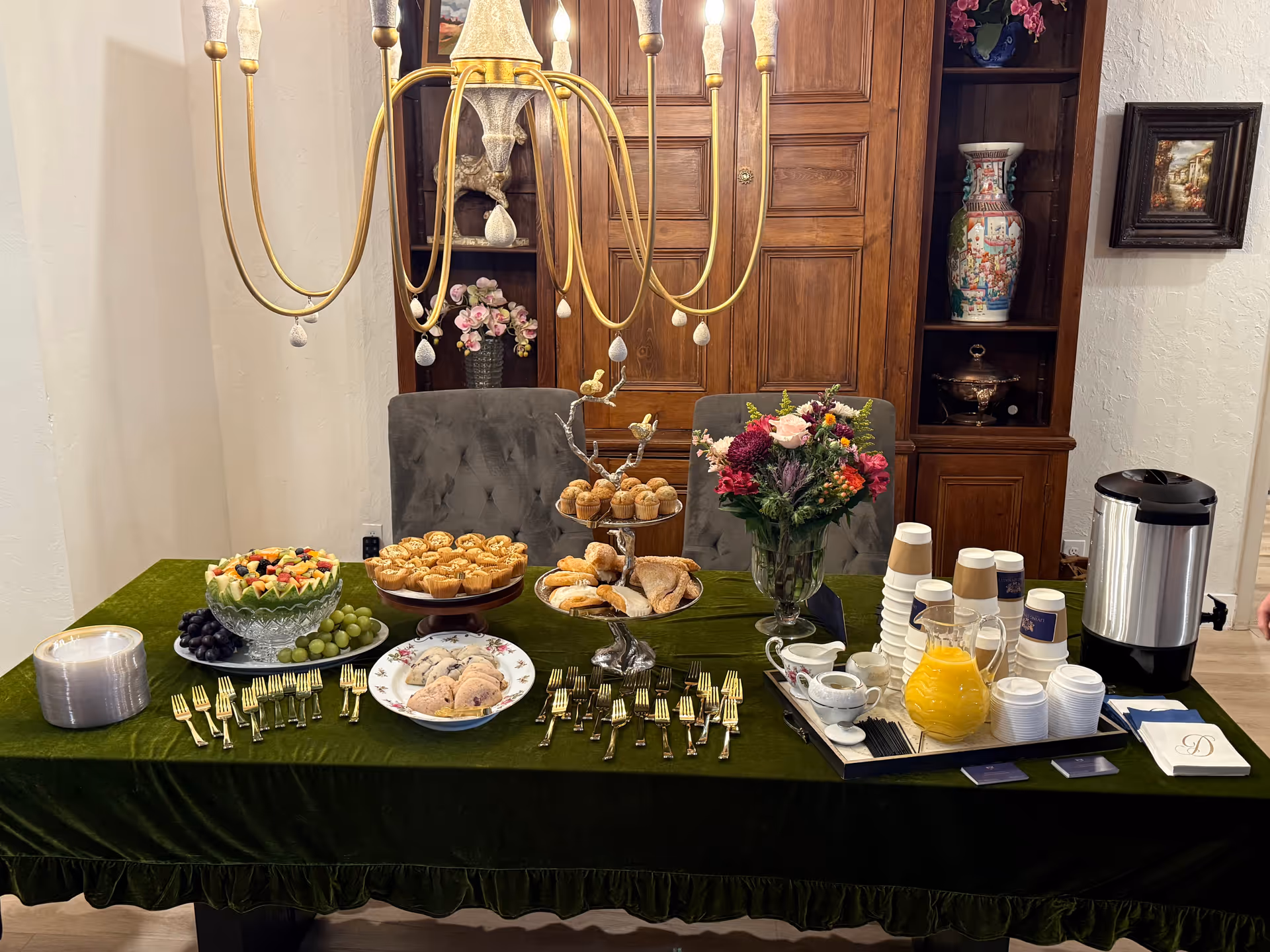 Long dining table with pastries, fruit, flowers, and a coffee setup in a dining room