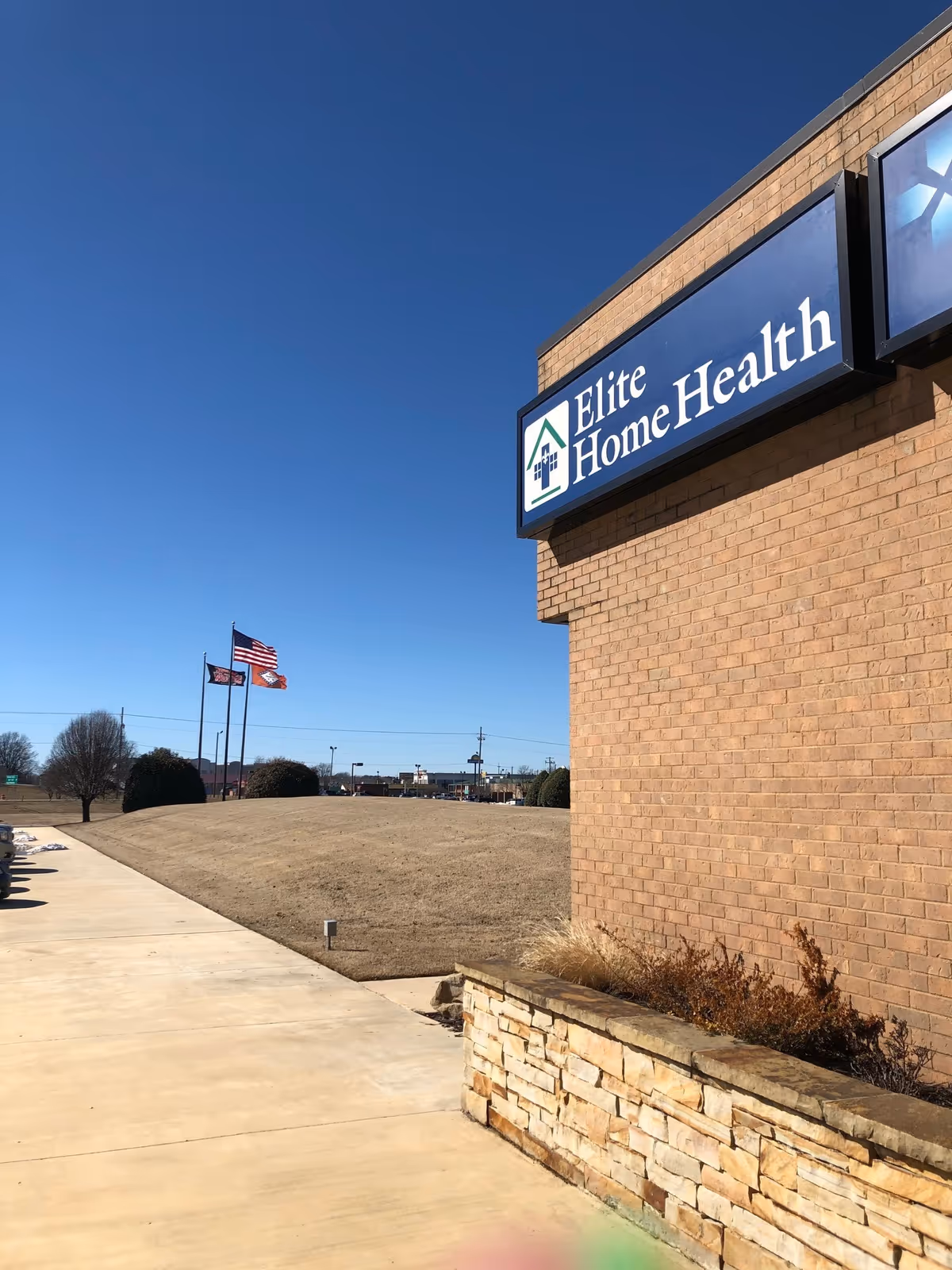 Exterior view of Elite Home Health facility sign on brick wall under blue sky.