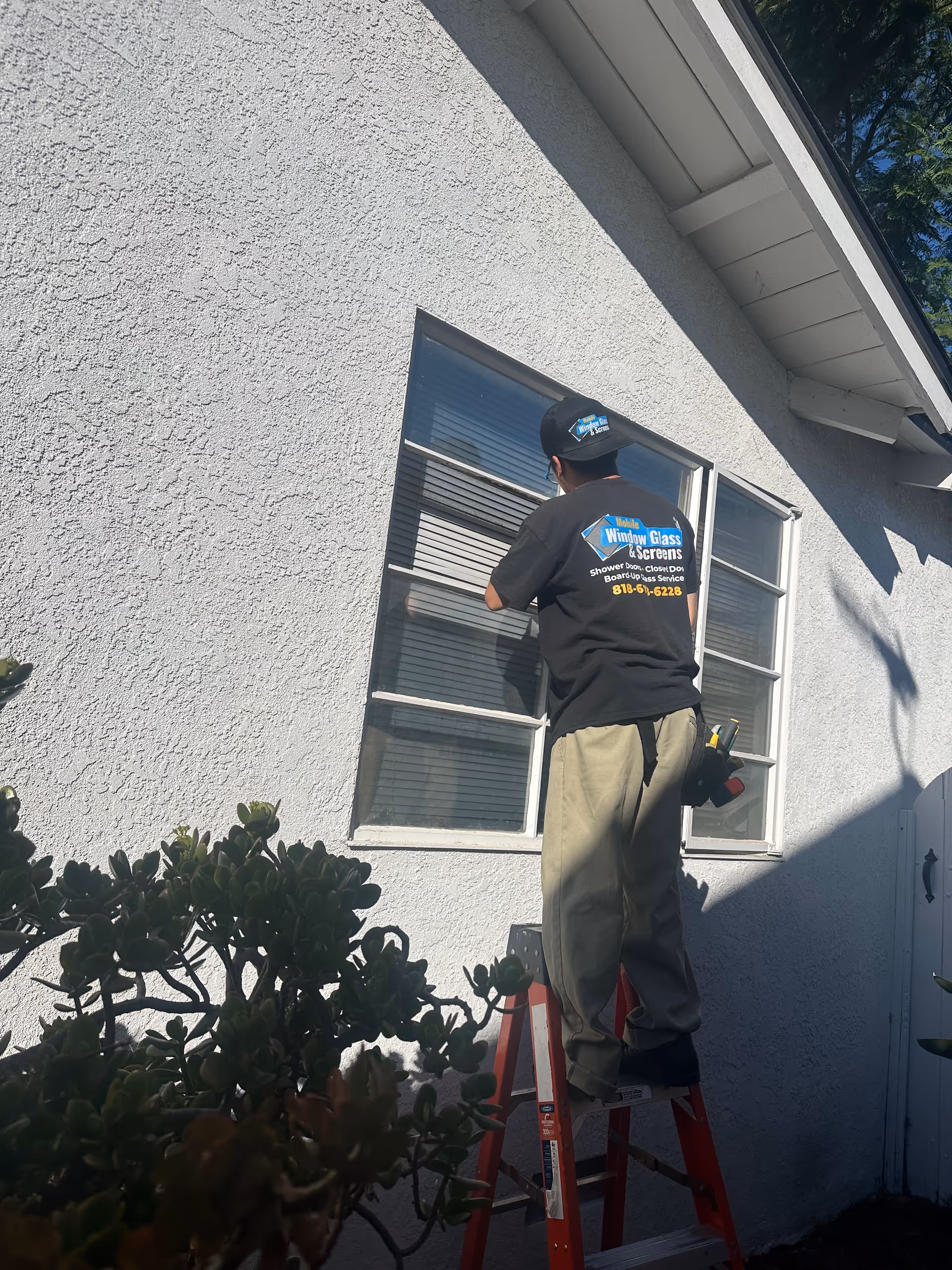 A maintenance worker on a red ladder cleans a window on a white exterior wall.