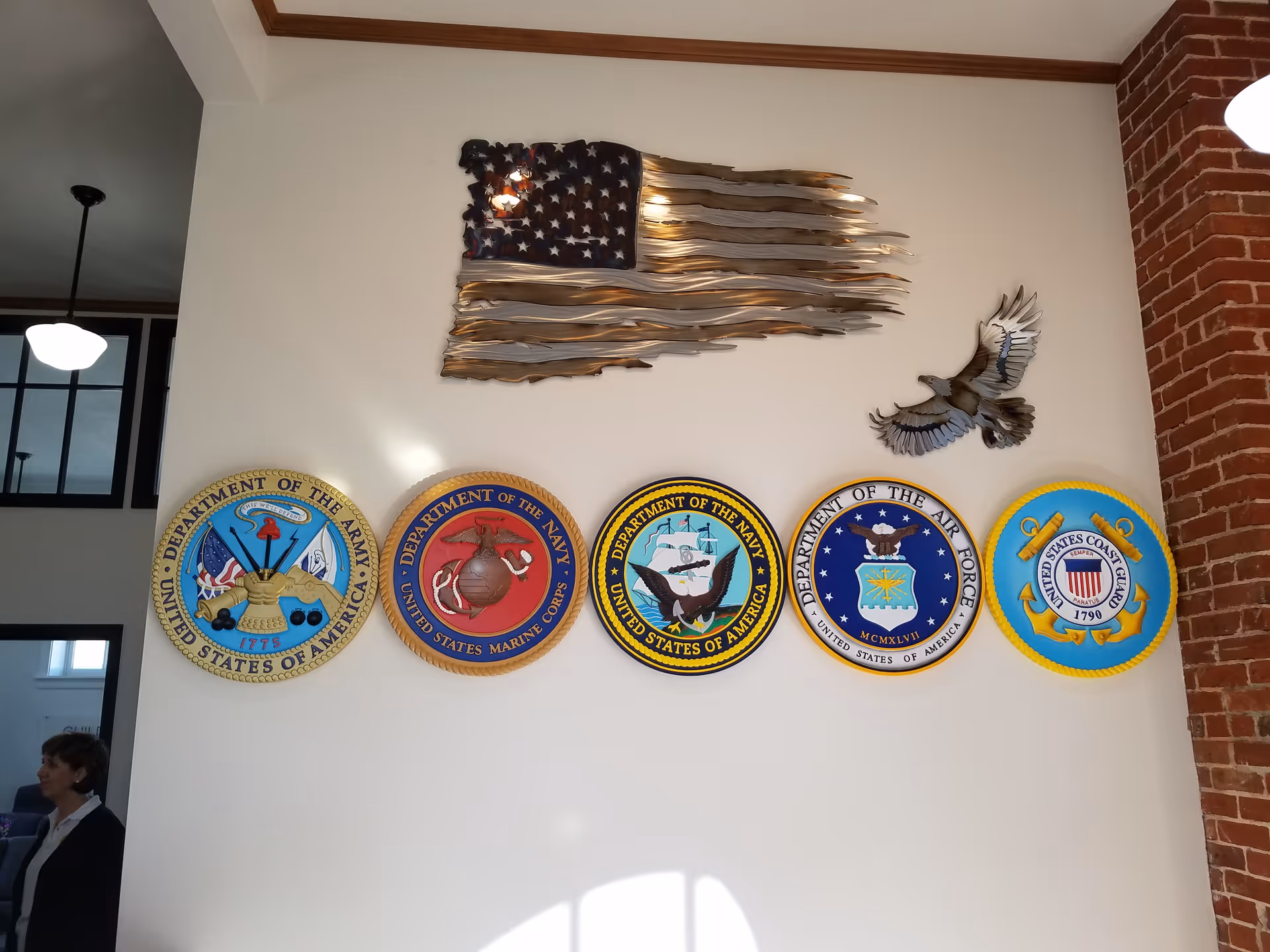 Interior wall displays military insignia plaques, American flag sculpture, and a brick column.