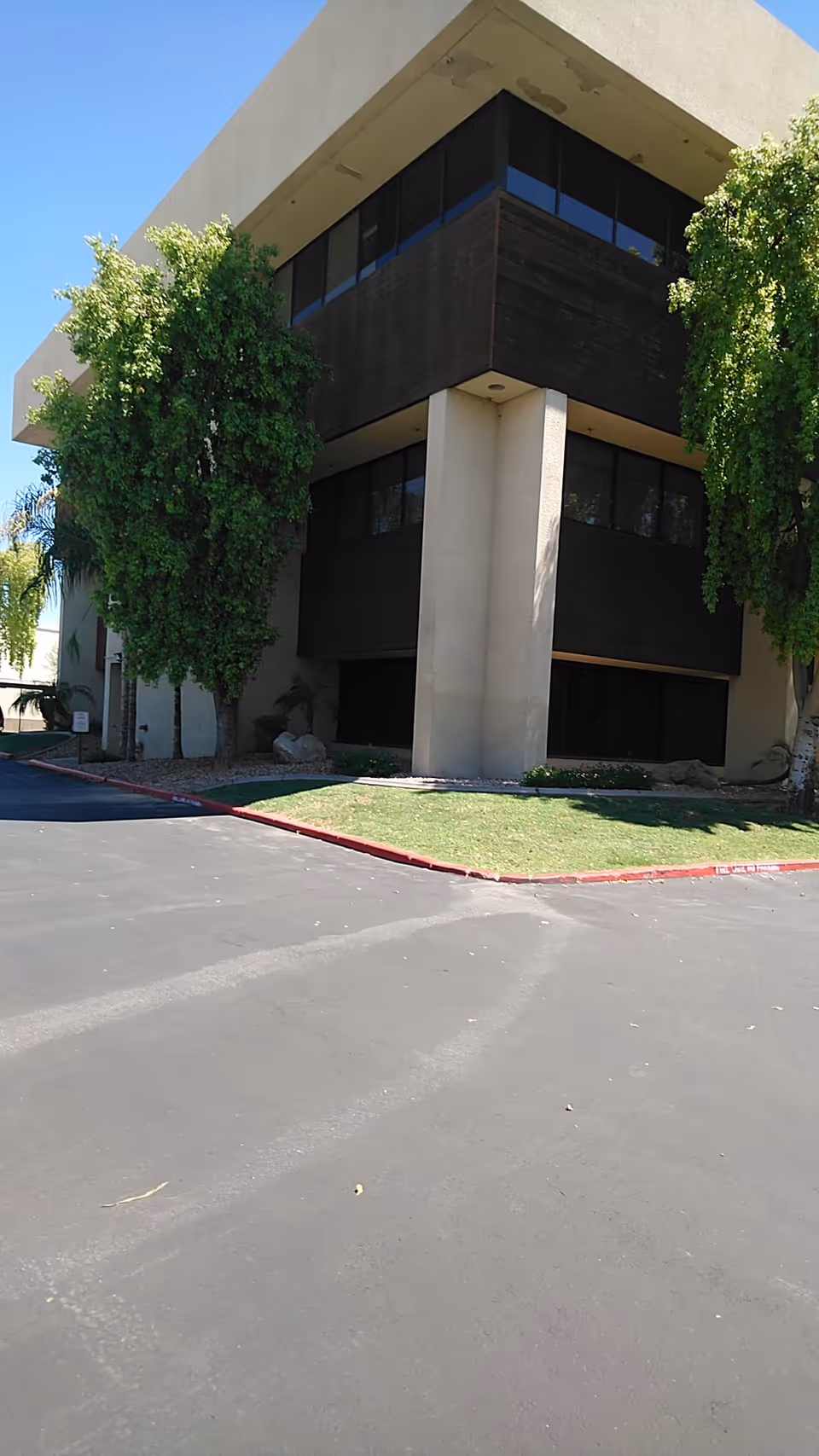 Modern multi-story building exterior with tall concrete columns, dark panels, and surrounding trees.