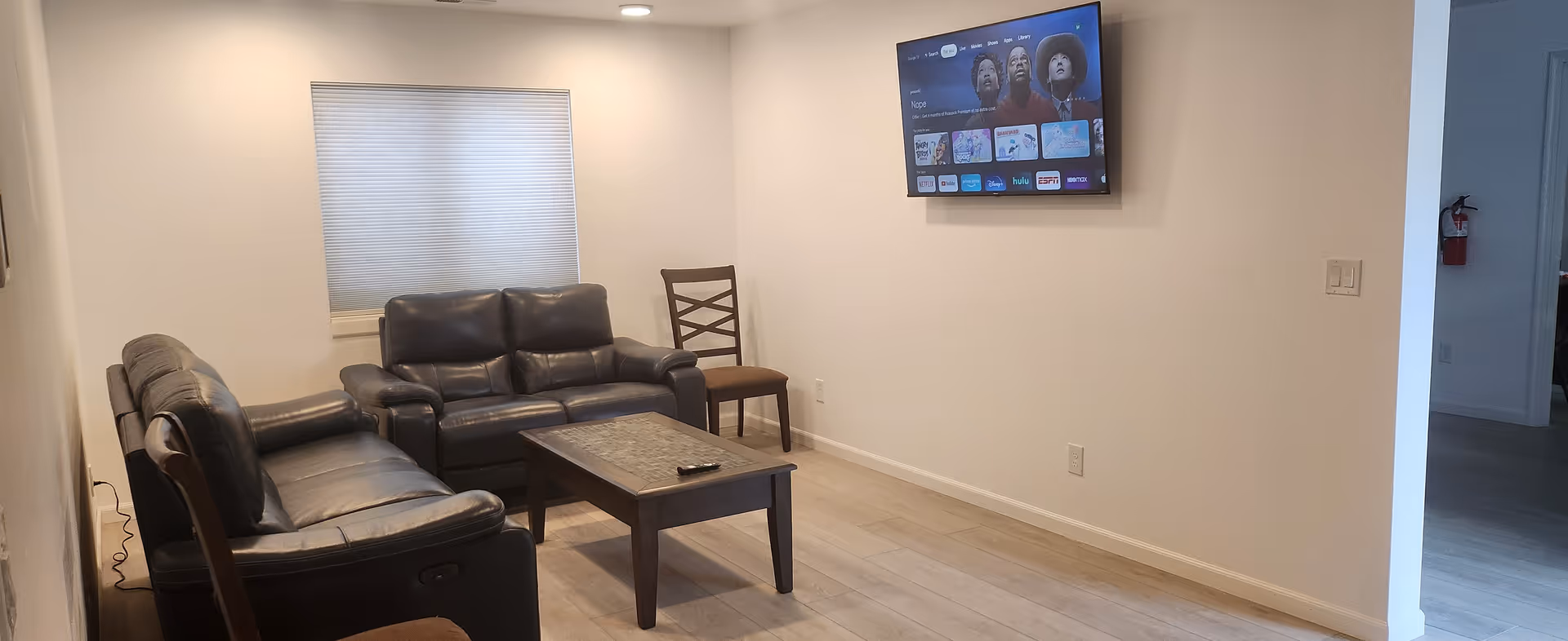 Modern living room in a senior facility with black leather seating and a wall-mounted TV.