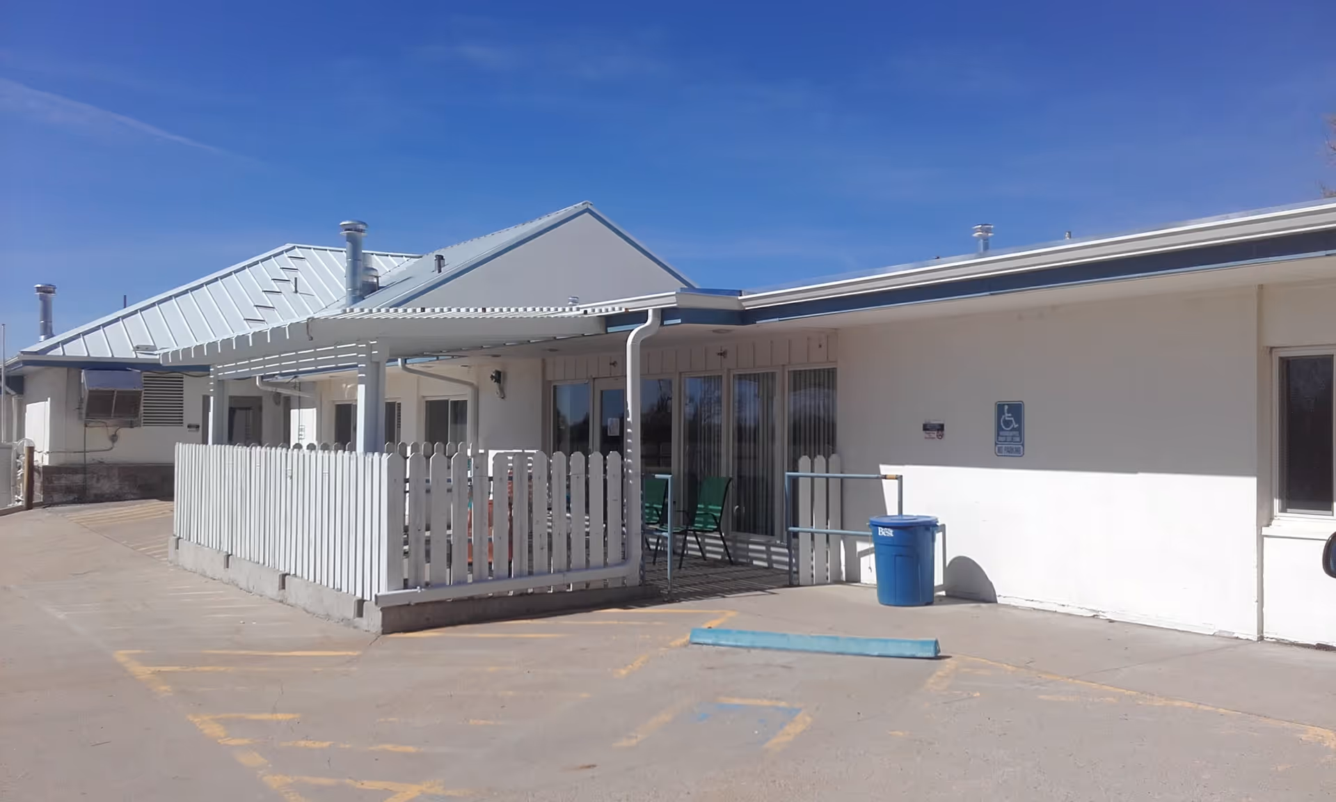 Exterior view of a single-story facility with a covered porch, white fence, and accessible entrance.