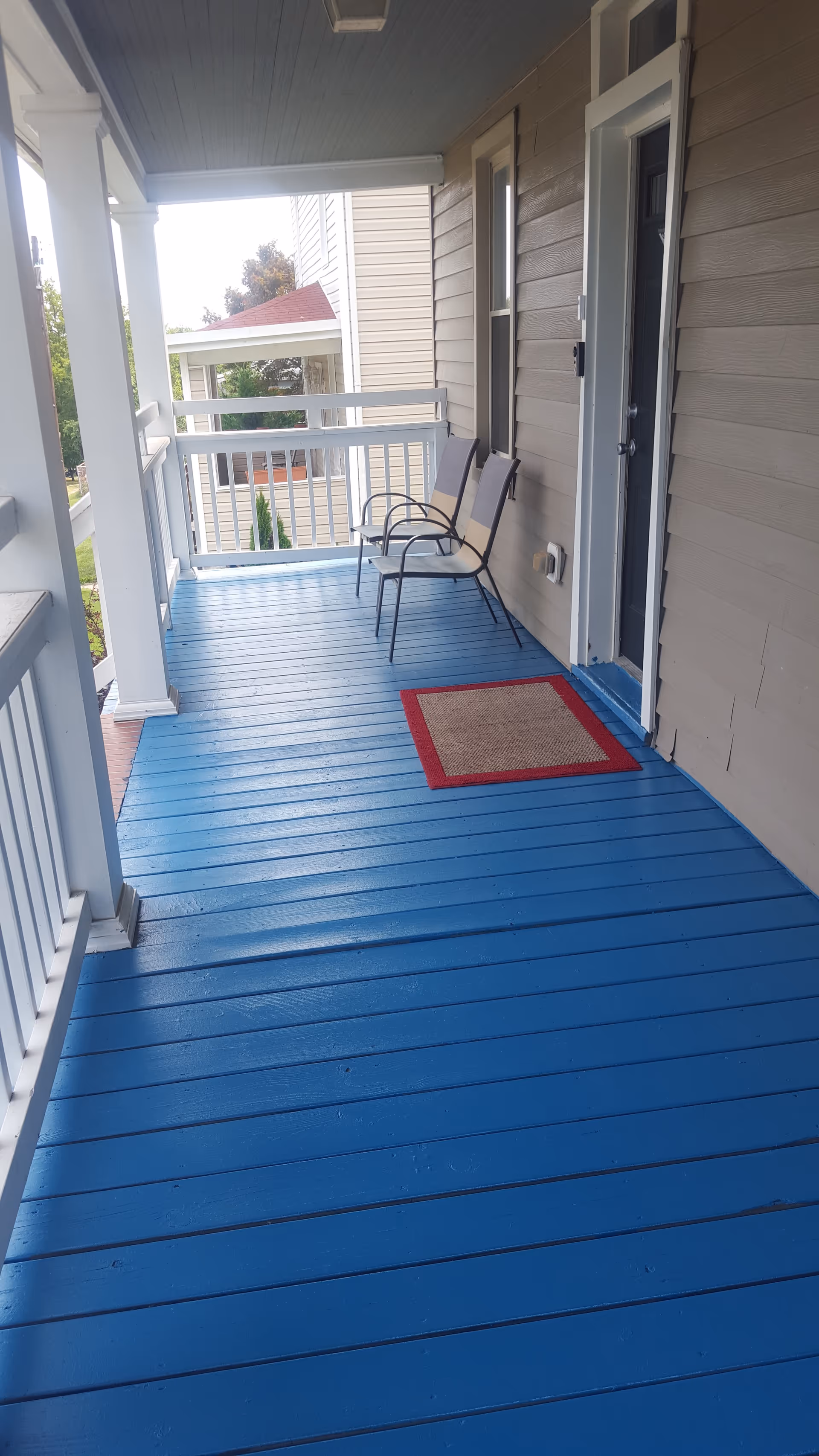 Blue-painted porch deck with two chairs outside a beige home.