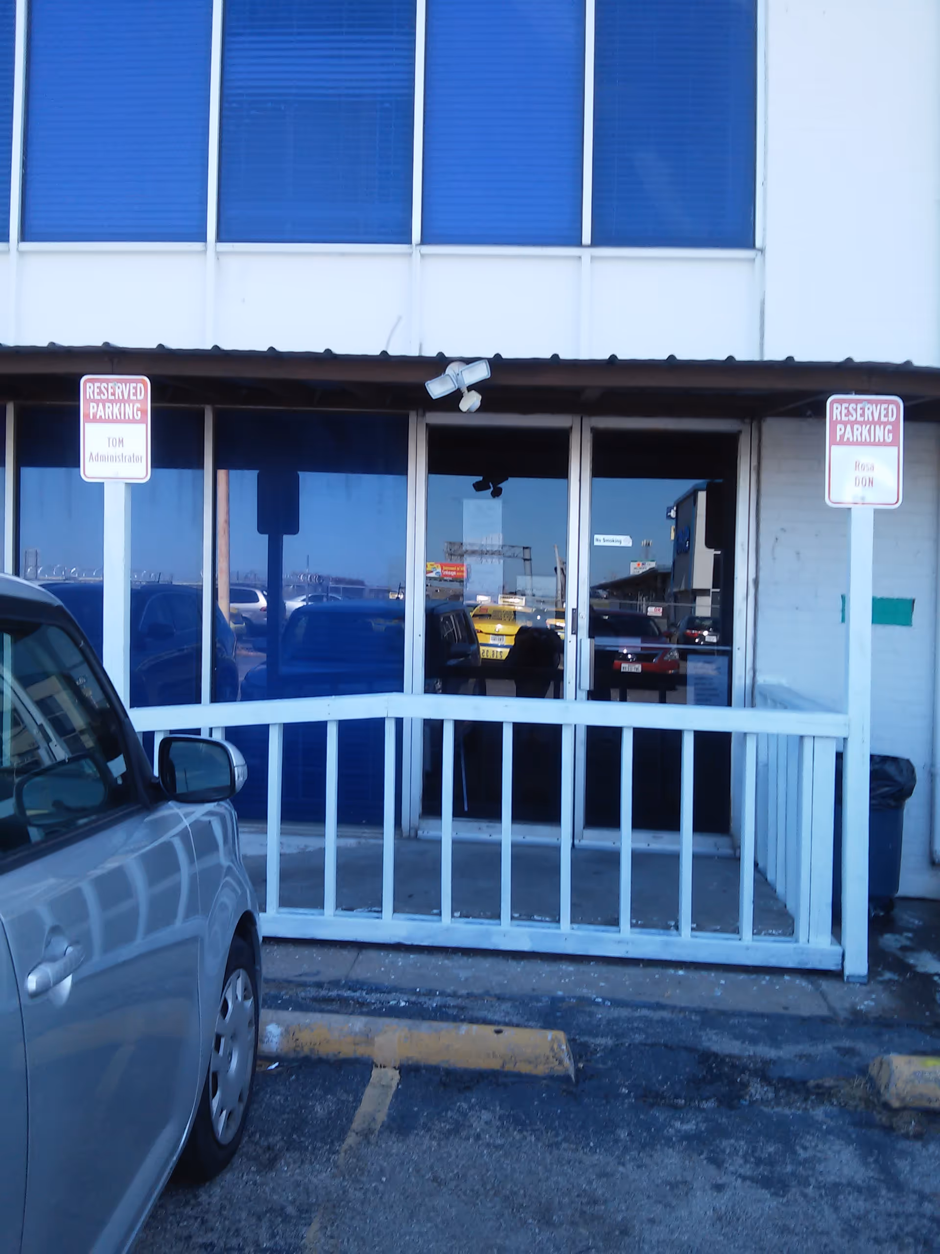 Front entrance of Affordable Elder Care building with glass doors, white railing, and reserved parking signs.