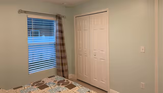 A small bedroom with a patchwork quilt on the bed, a window, and closet doors.