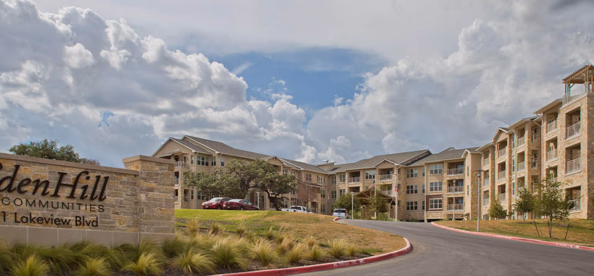 Exterior view of the EdenHill Communities senior living building and entrance with a stone sign, curved driveway, and cloudy sky.