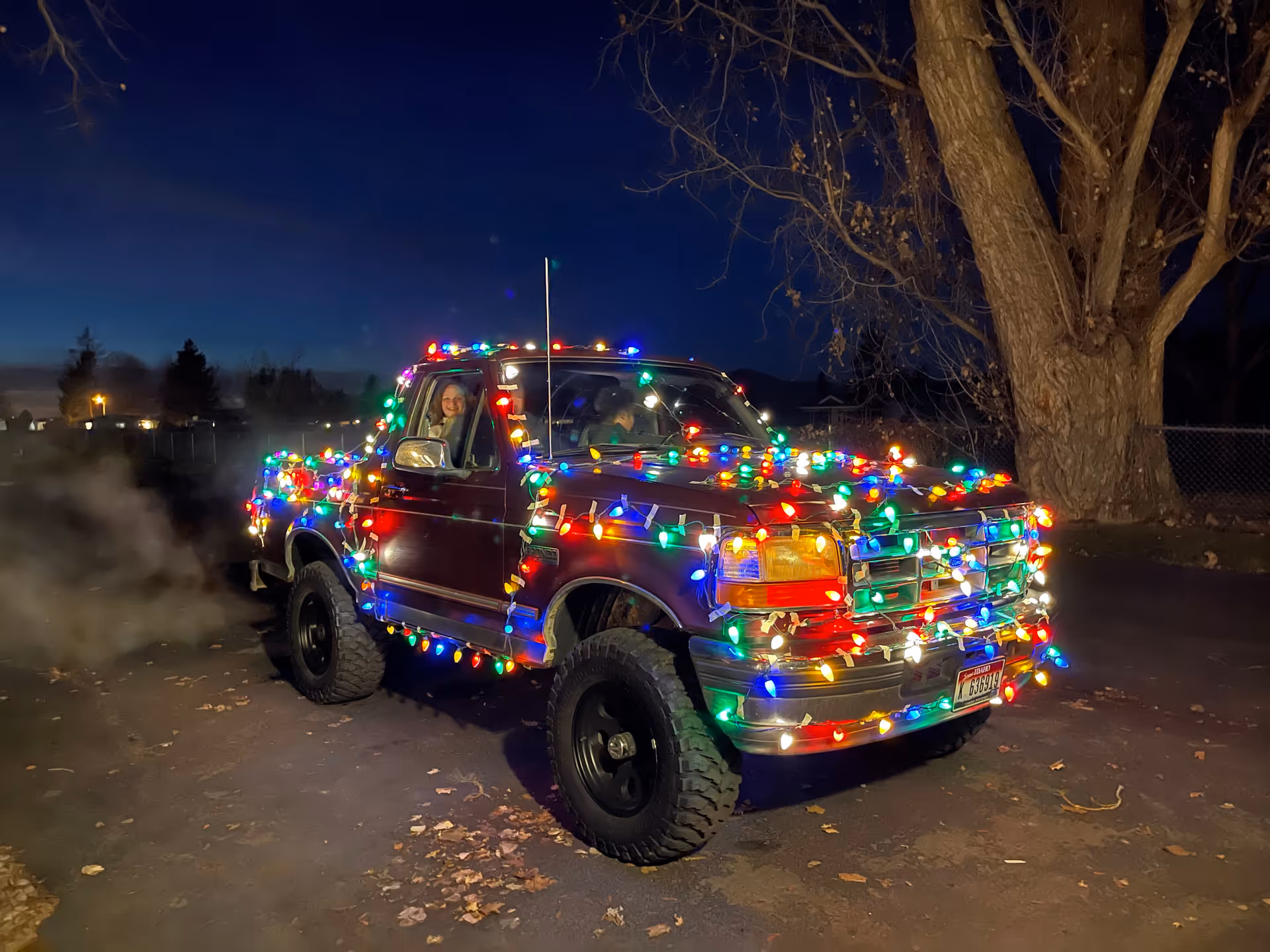 Pickup truck adorned with colorful Christmas lights parked outdoors at night.