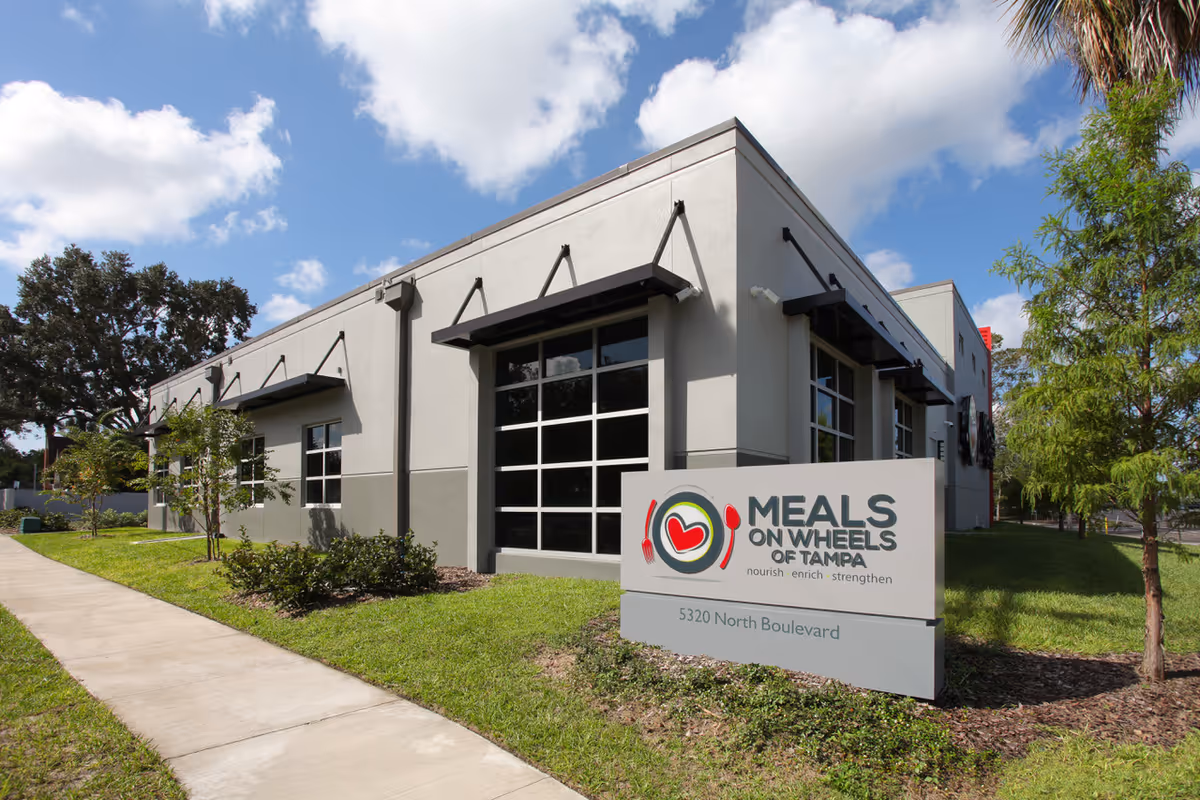 Front exterior of a Meals On Wheels of Tampa facility with sign and walkway.