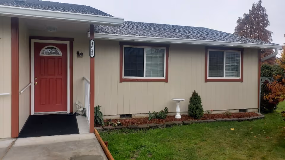 Front exterior of a single-story home with beige siding, red door, and small garden
