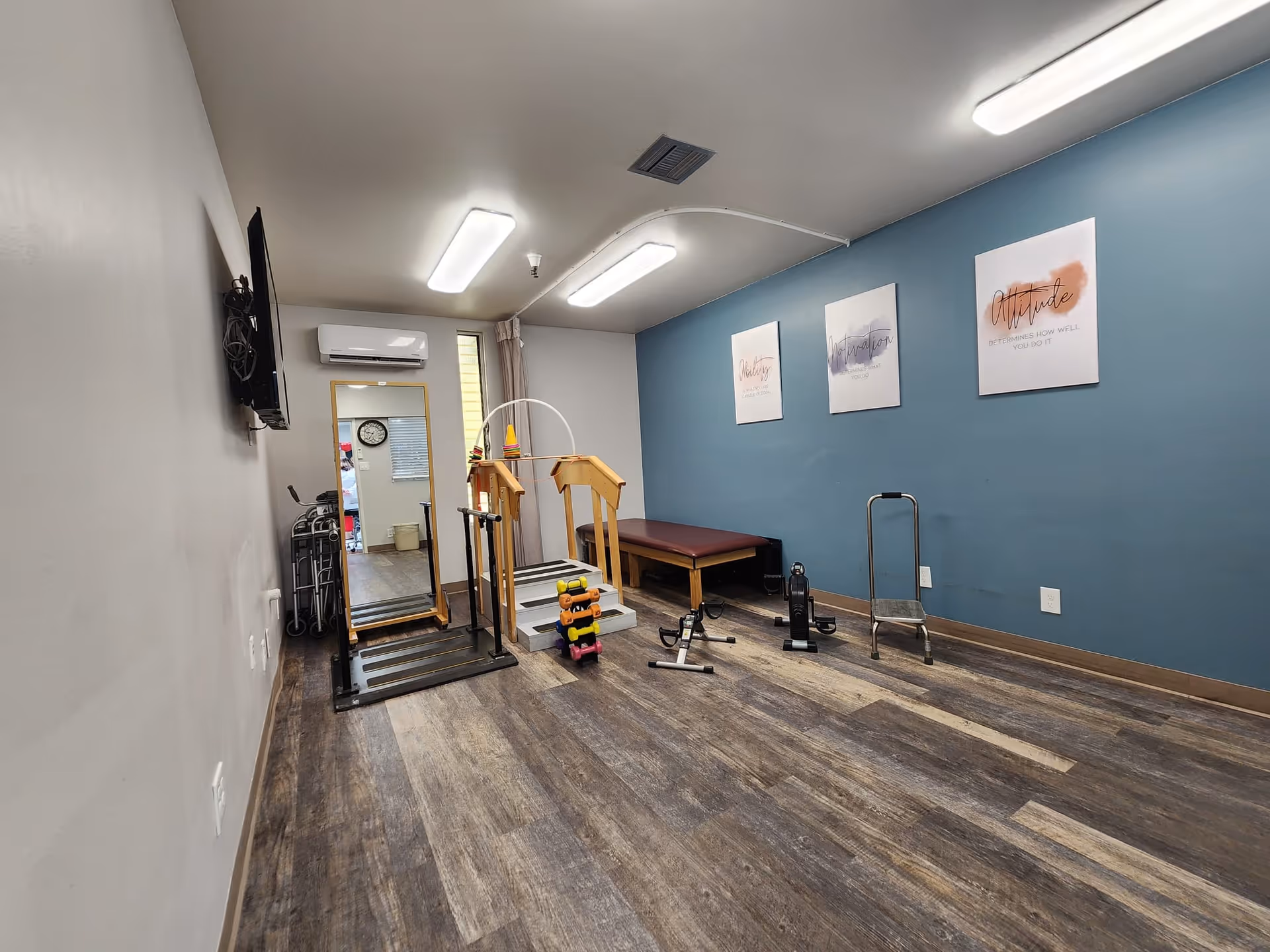 Interior fitness room with exercise equipment, blue accent wall, and mirrors in a senior living facility.
