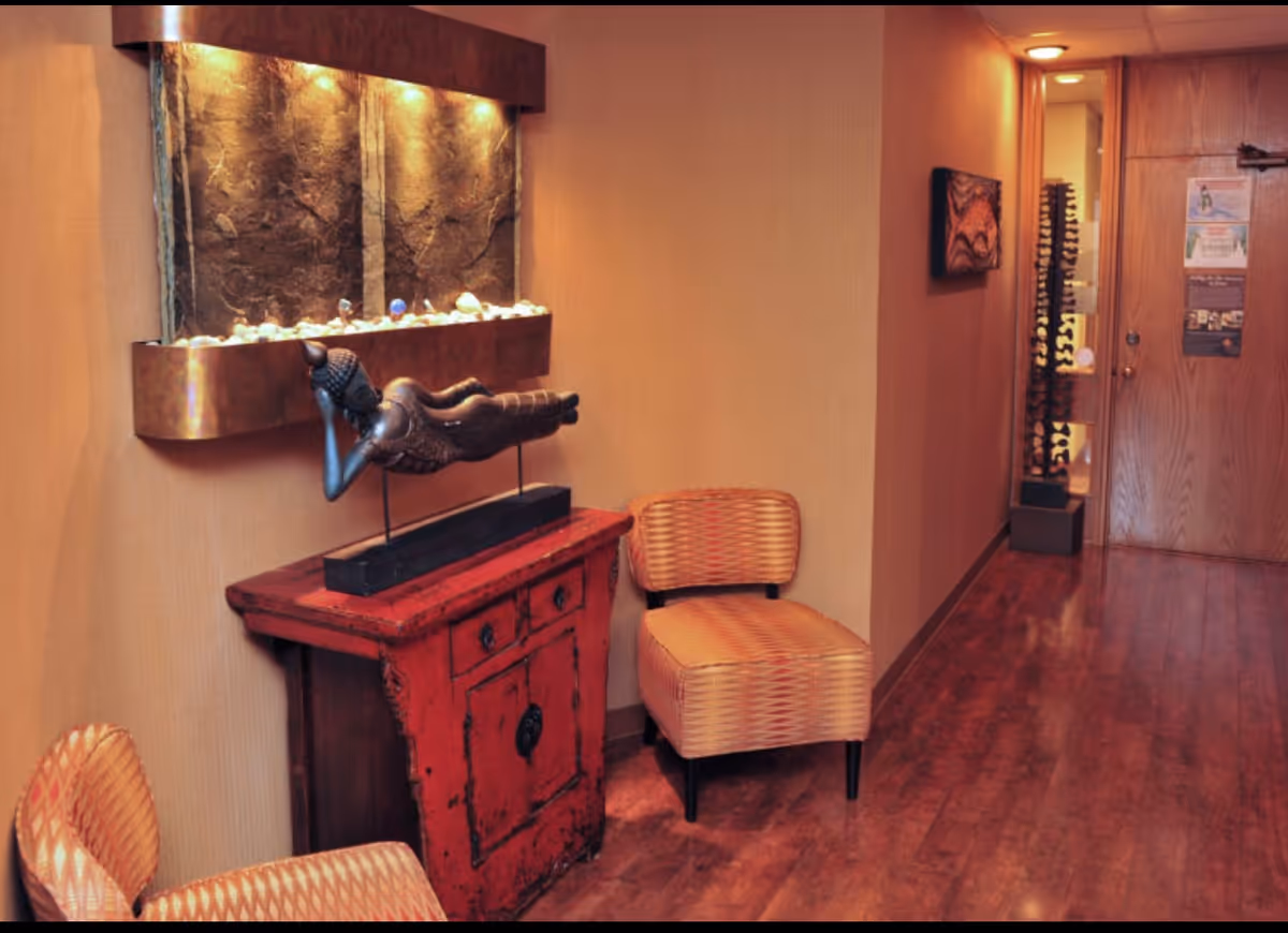Interior hallway with wooden floor, wicker chair, red cabinet, and wall-mounted water feature.