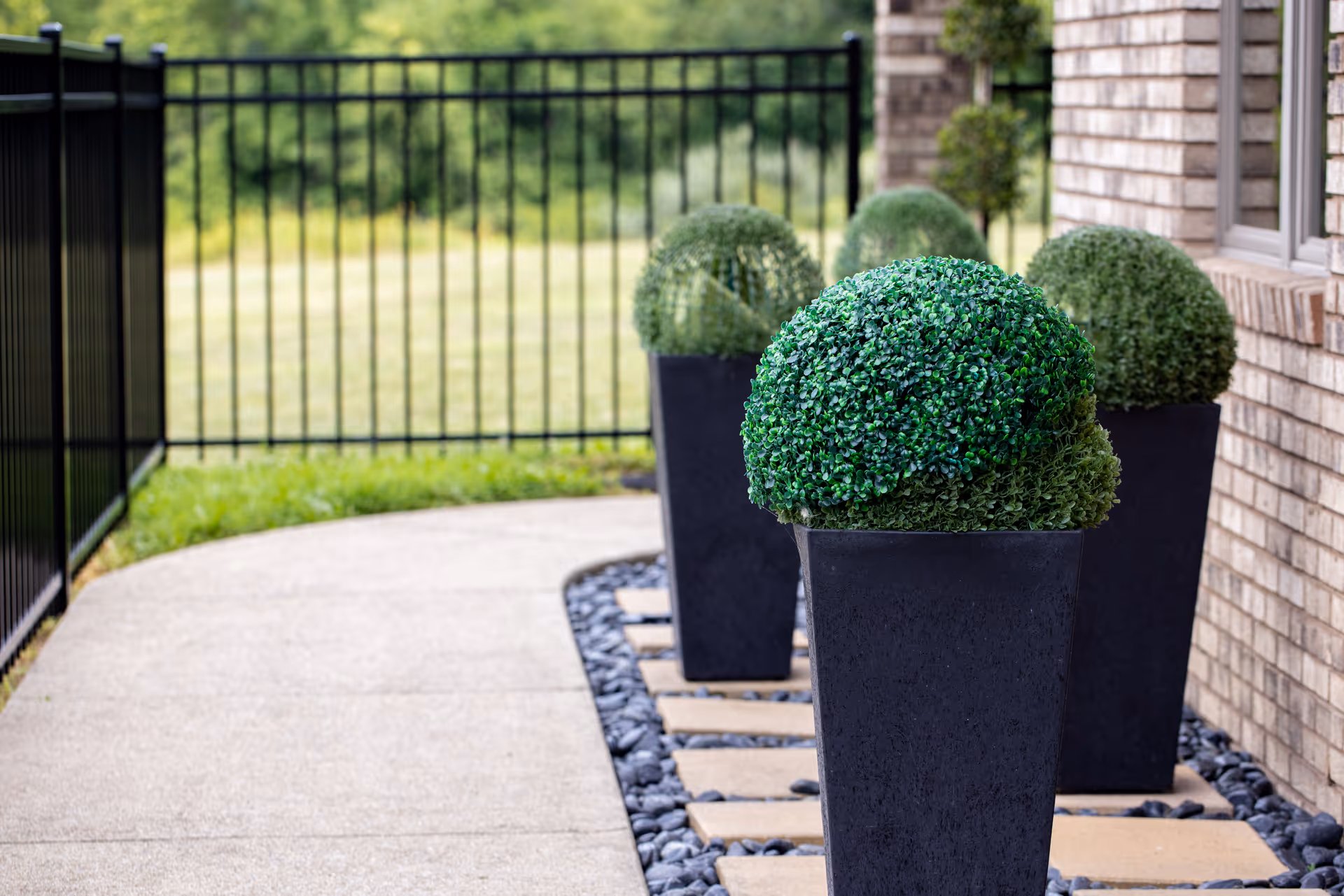 Exterior walkway with tall potted topiary plants along a brick building.