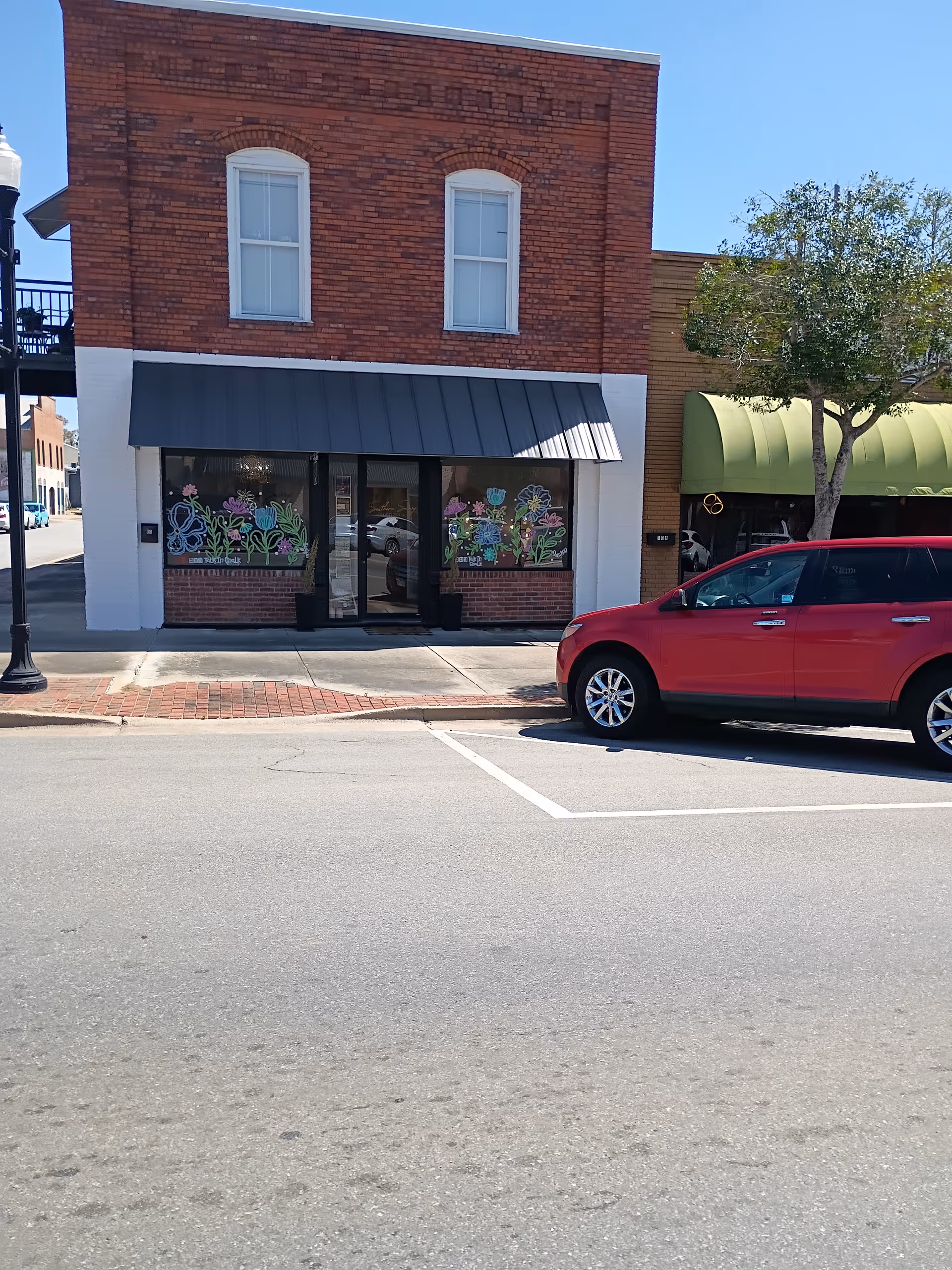 Two-story brick building with storefront and black awning; a red SUV is parked outside.
