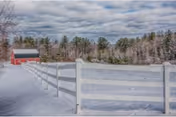 Snowy outdoor scene with a white fence and a distant red barn.