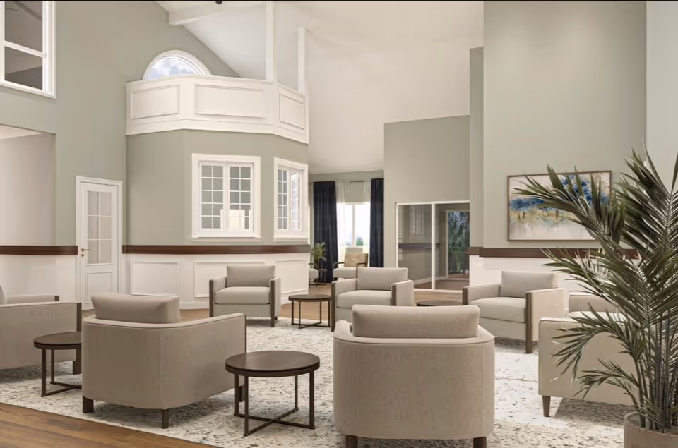 Spacious senior living lounge with beige seating, round tables, and greenery.