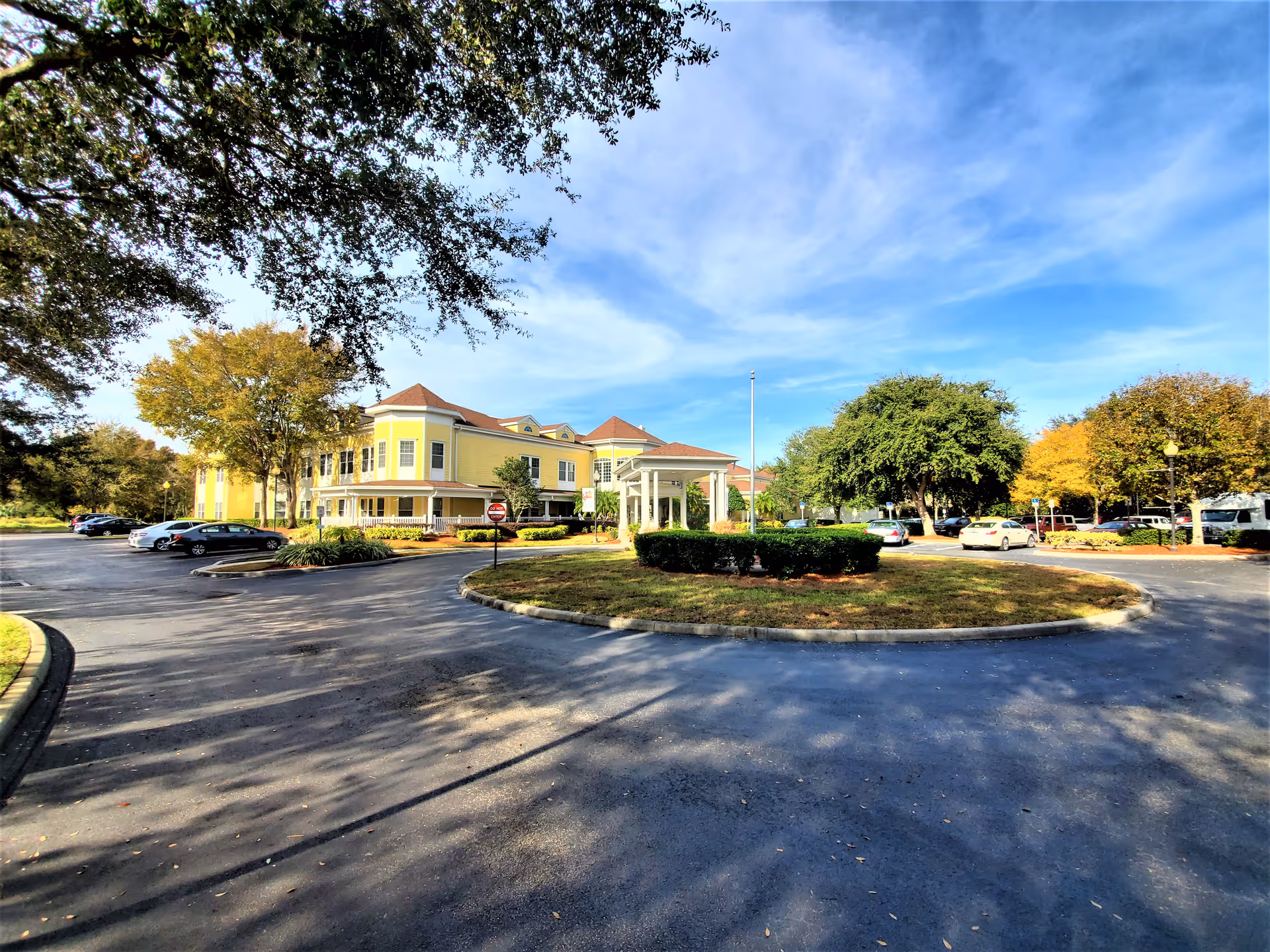 Yellow two-story senior living building with circular drive and surrounding trees.