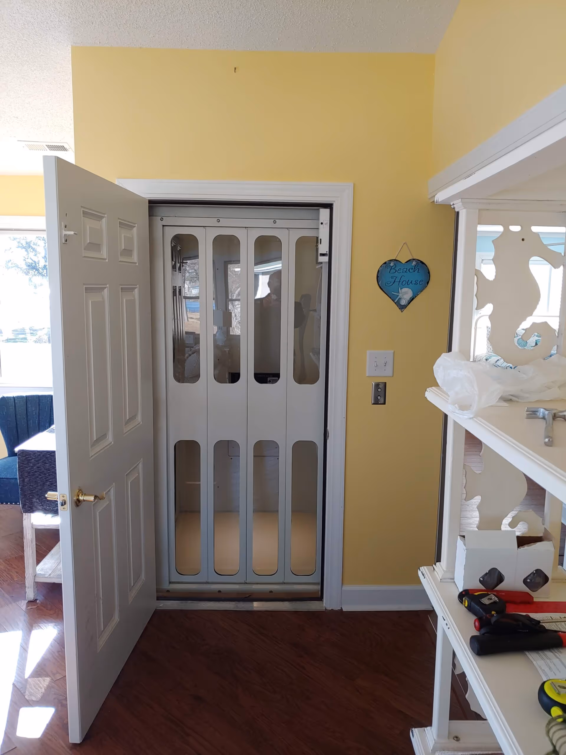 Inside a yellow-walled room, a small vertical elevator with glass-panel doors is visible.