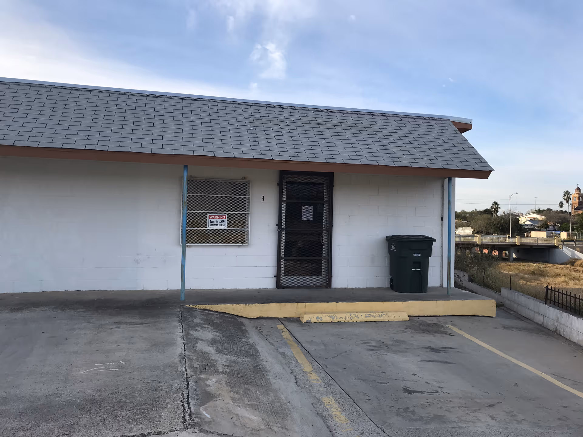 Front view of a small single-story facility with barred window, door, and parking lot.