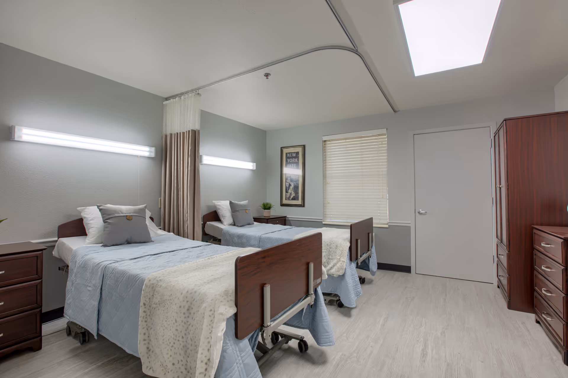 Two beds in a shared resident room with curtains, dressers, and soft lighting.