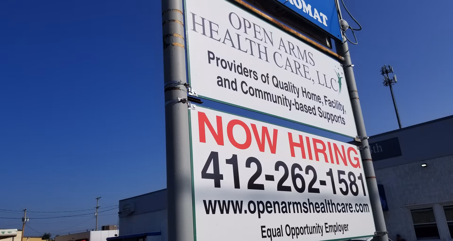 A tall outdoor sign advertising Open Arms Health Care with Now Hiring.