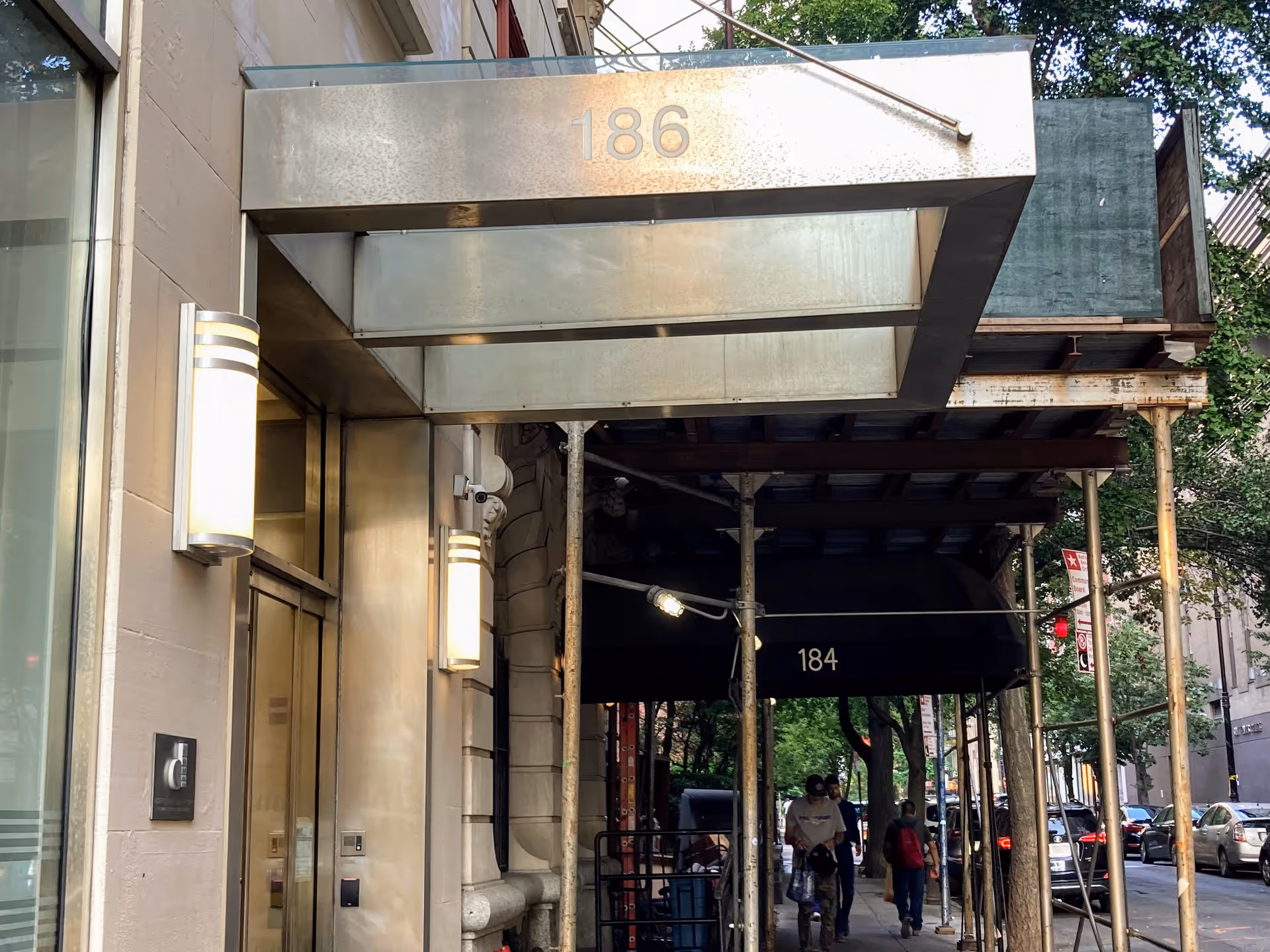Exterior building entrance with metal canopy labeled 186 and scaffolded street frontage.
