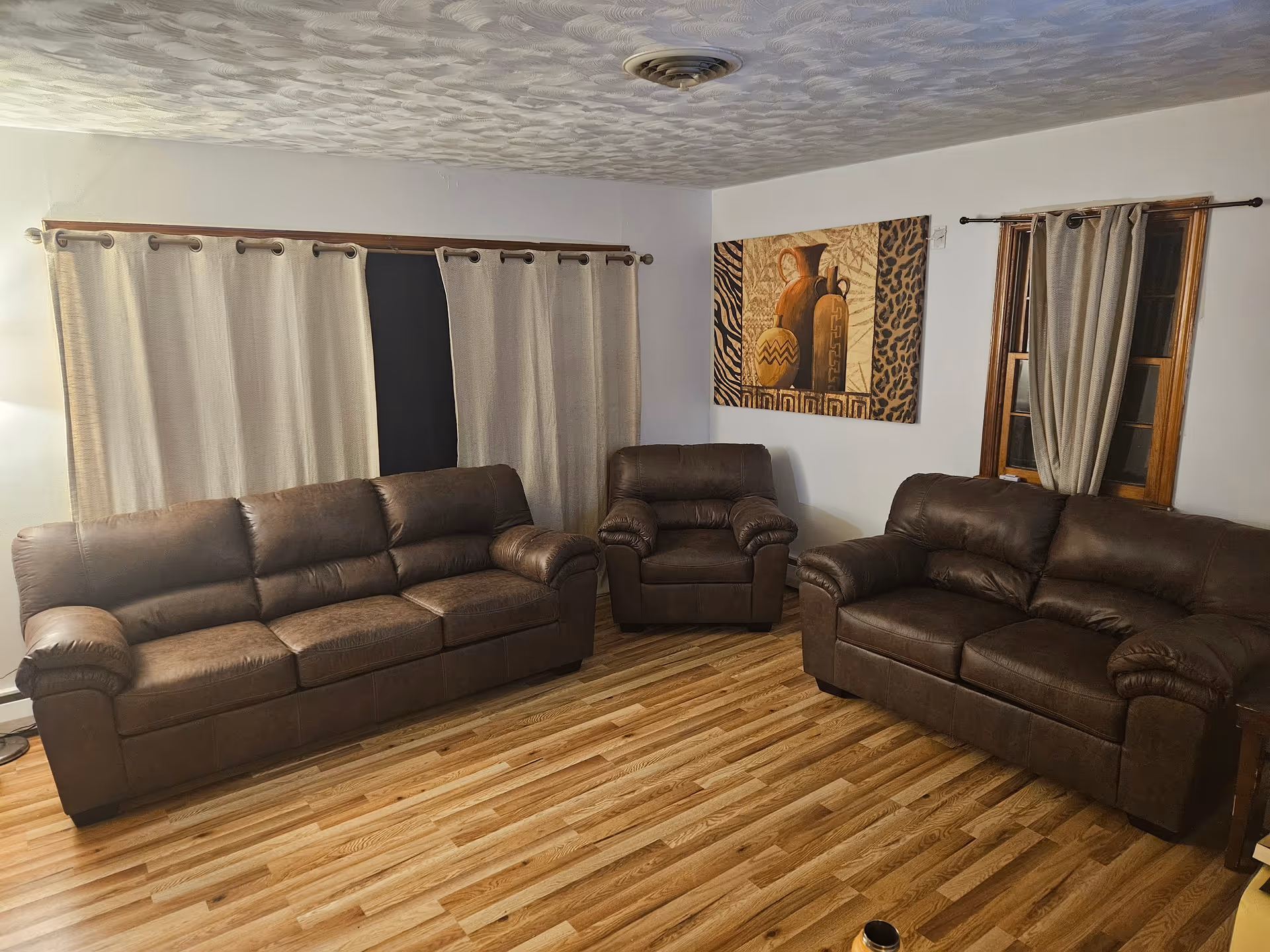 Brown leather sofas arranged in a cozy living room with curtains and wall art.