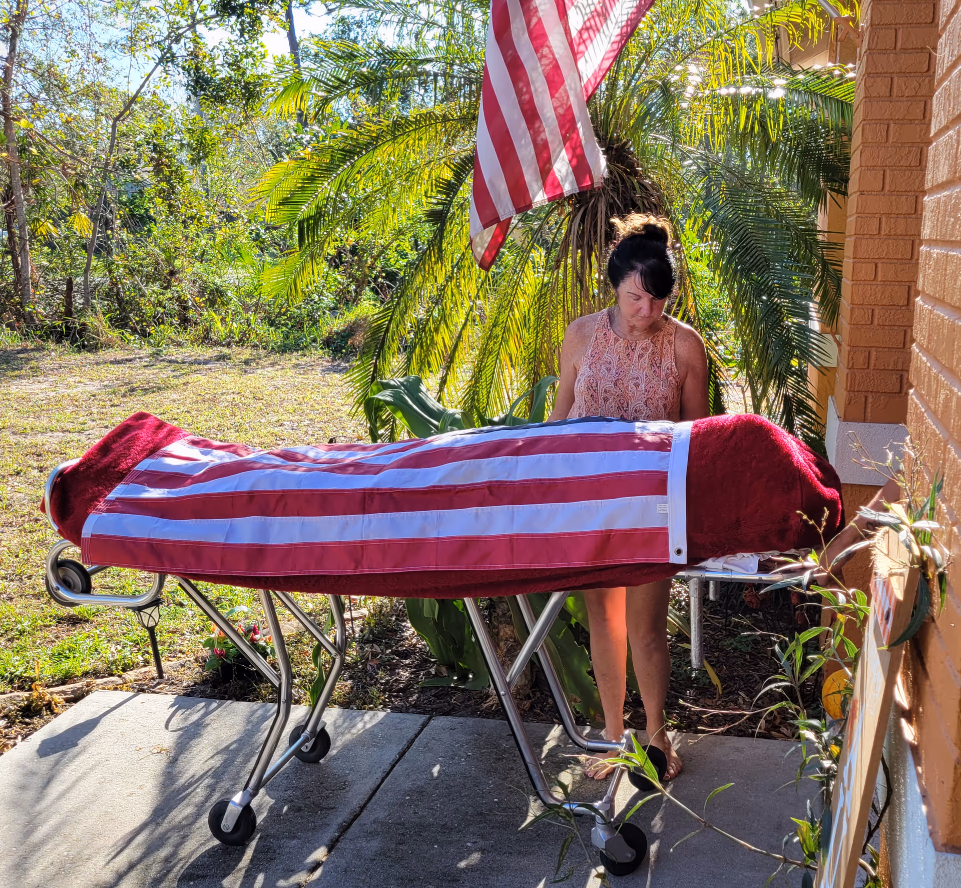 A woman stands beside a flag-draped coffin on a wheeled gurney outside.