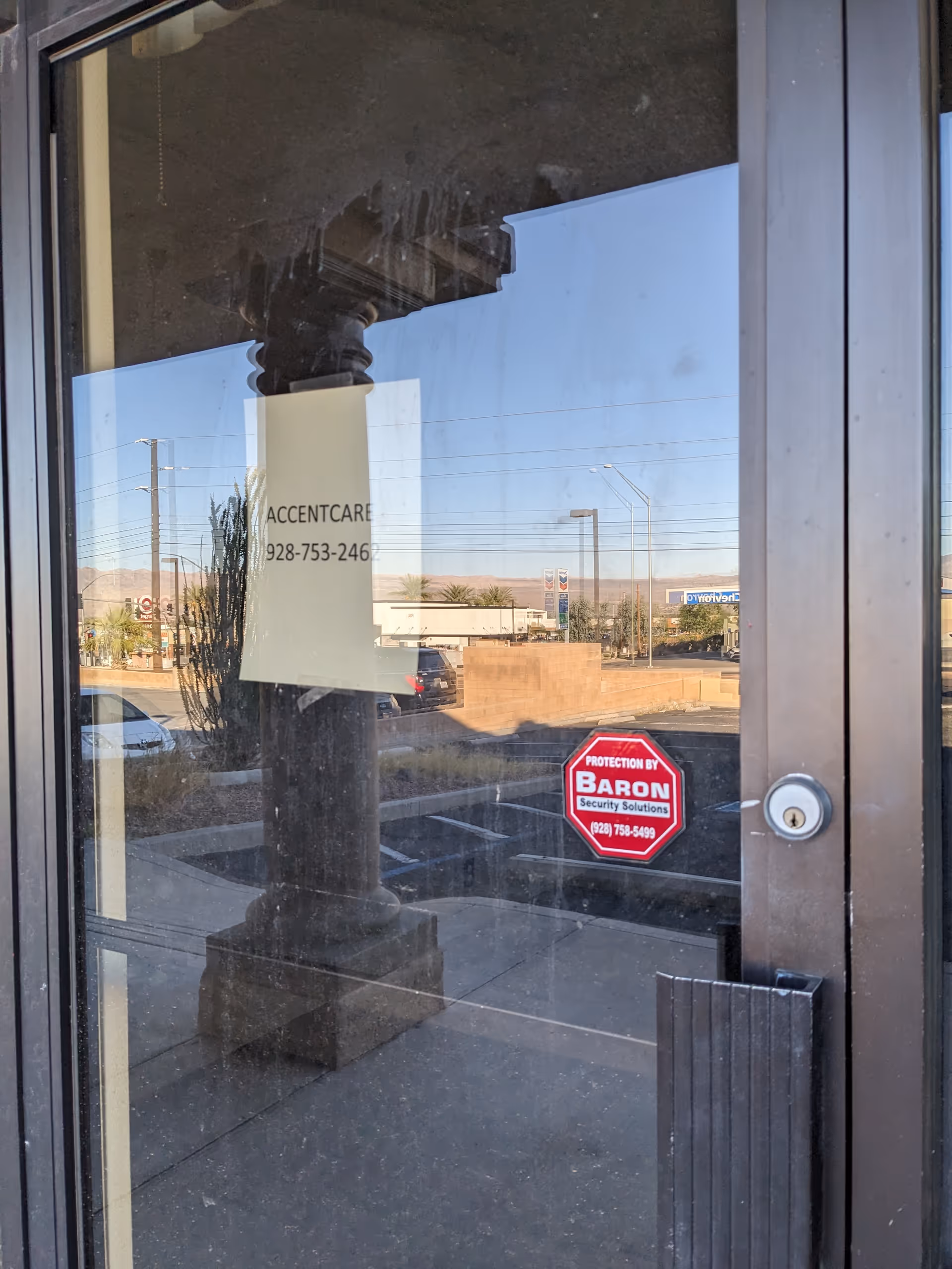 Glass entrance door with AccentCare sign and a security sticker, reflecting the parking lot outside.