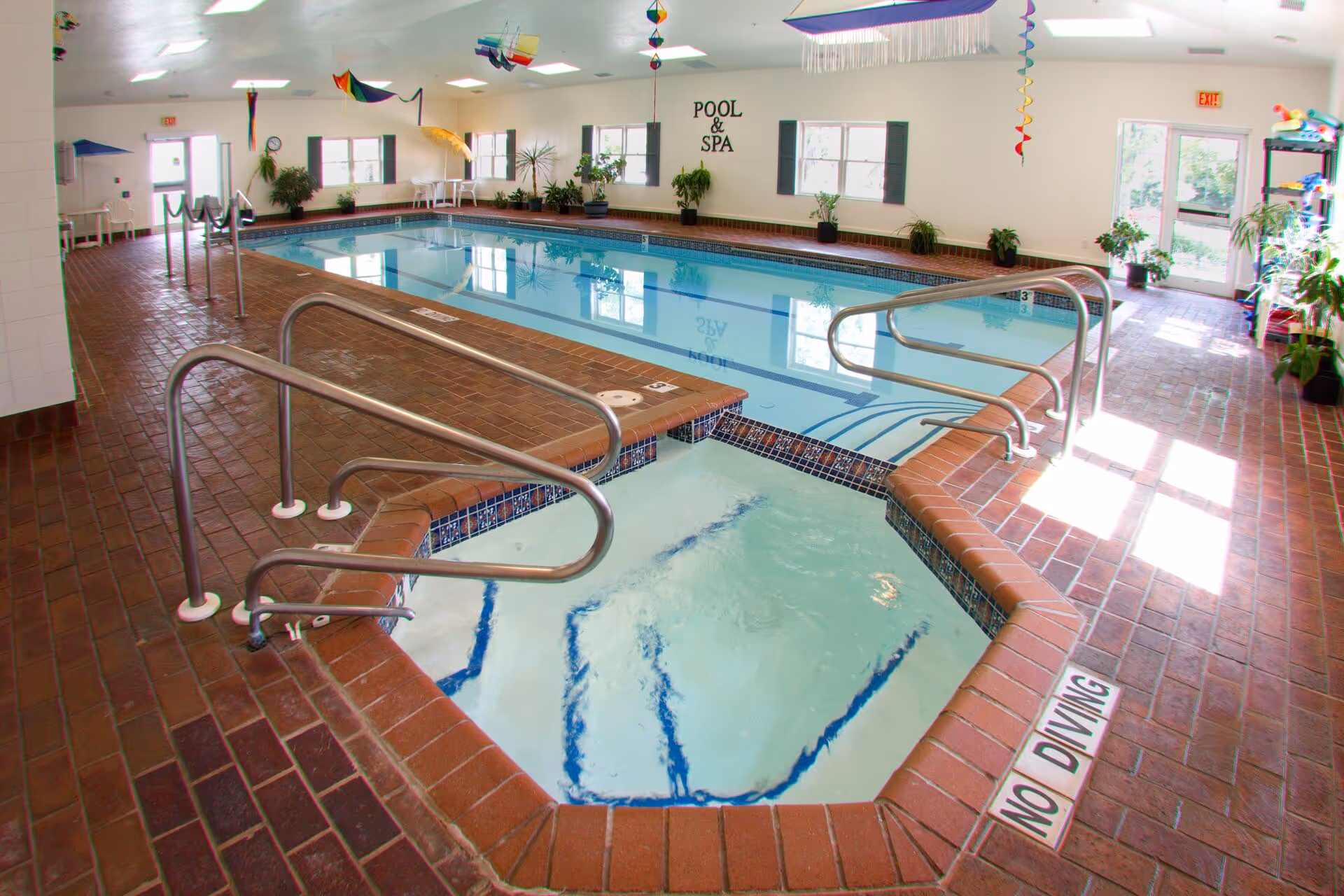 Indoor pool area at The Inn at Freedom Village with pool, spa, brick flooring, and plants.