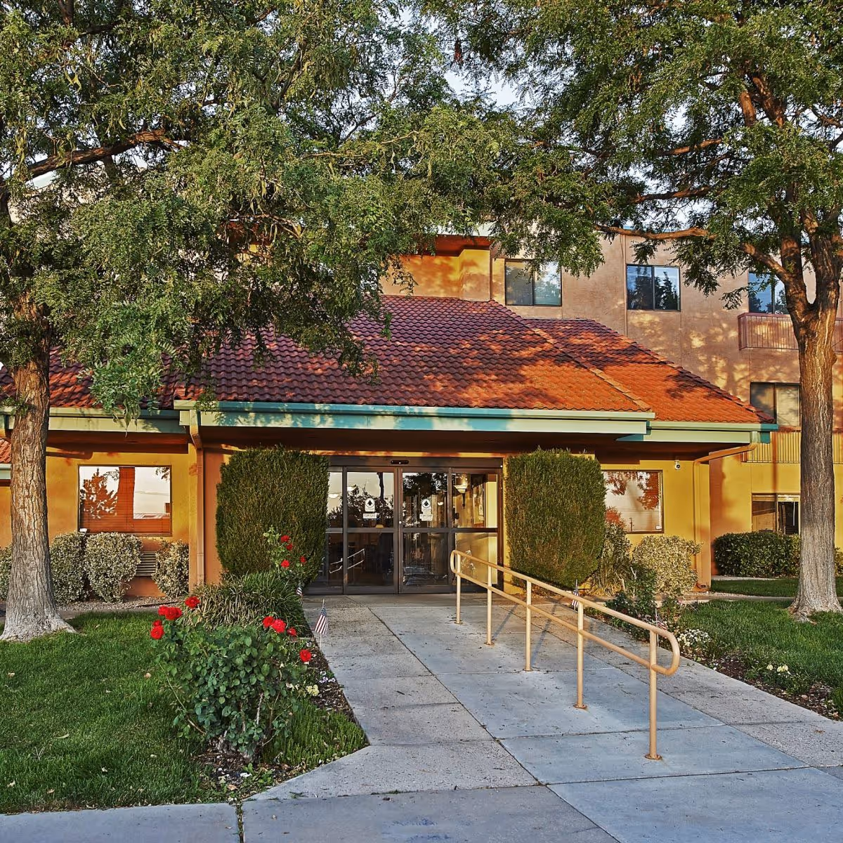 Sandia Vista Senior Living entrance with red-tiled roof, ramp, and manicured landscaping.