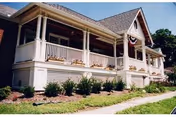 White, porch-front senior living house with railing, shrubs, and a sloped roof.
