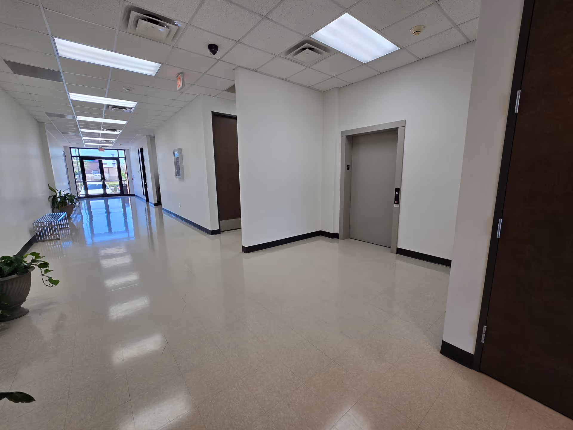 Long, clean hallway inside a senior living facility with elevator, plant decor, and seating.