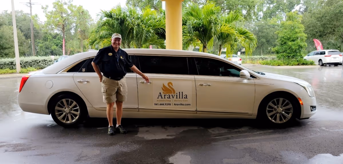 A man in uniform stands beside an Aravilla car in a rainy parking lot.
