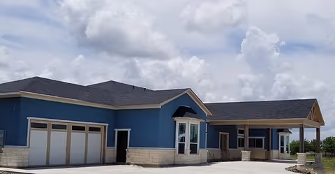 Blue single-story senior living facility exterior with covered entry and garage bays.