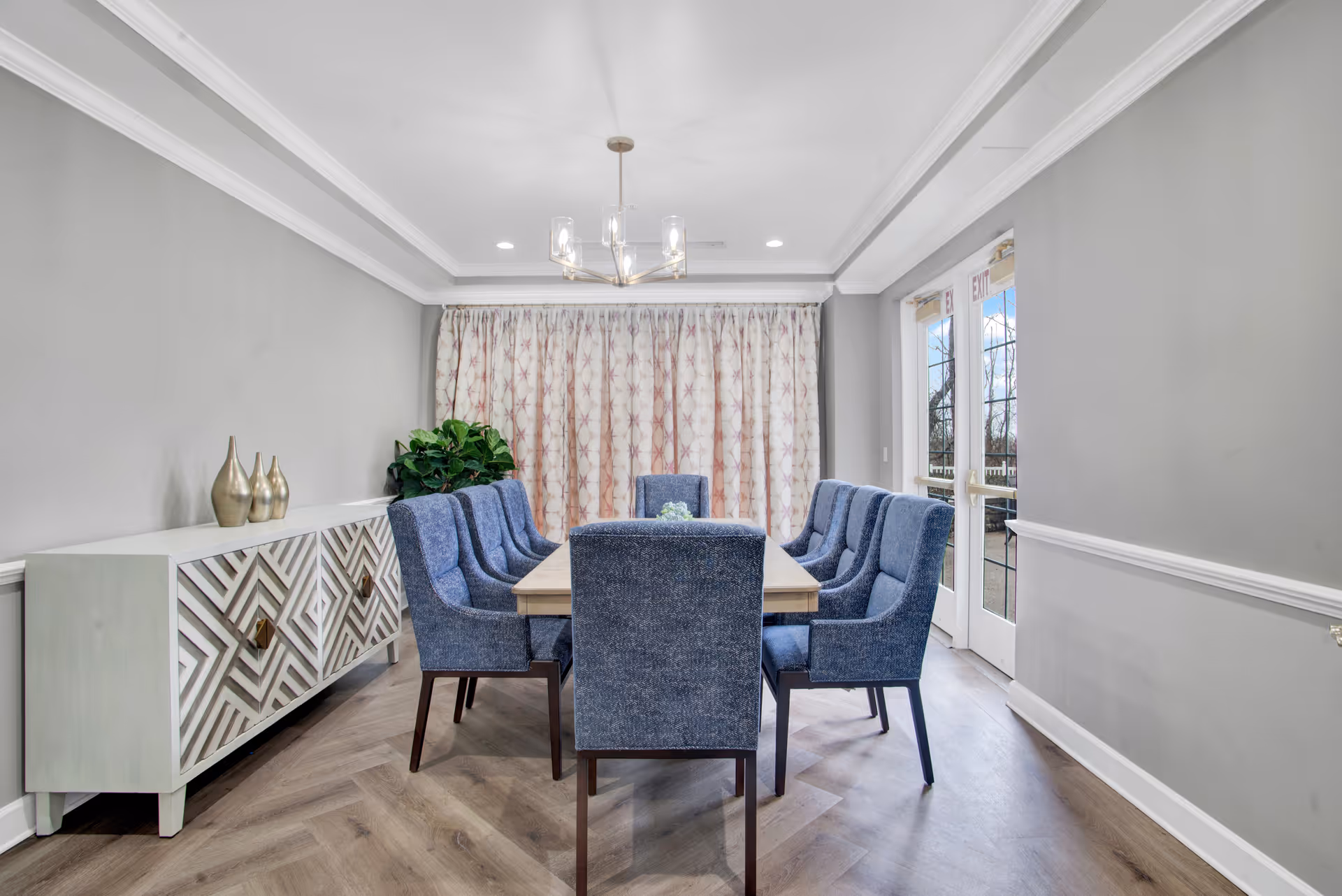 Gray dining room with a long wooden table surrounded by blue upholstered chairs.
