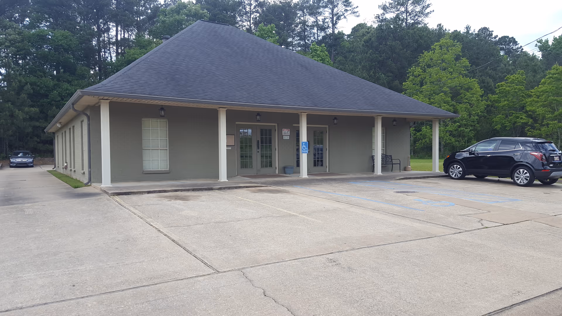 Single-story facility with covered entrance, handicap parking, and parked cars in driveway.